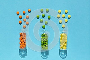 Colorful, orange, green, yellow pills spill out of the transparent bottle on the blue background.