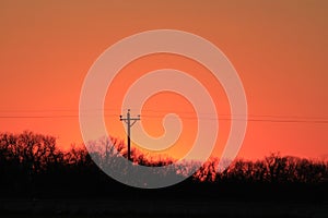 A colorful orange sky at Sunset with powerline silhouettes with trees in Kansas