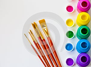 Colorful paint bottles and paint brushes on white background with copy space, top view/arts and crafts background concept