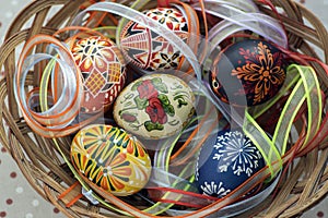 Colorful painted Easter eggs in brown wicker basket covered with colorful ribbons, traditional Easter still life