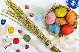 Colorful painted eggs in a nest of twigs of willow on a light background and multicolored rice for decorative painting