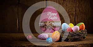 Colorful painted happy easter eggs in birds nest basket on rustic wooden old panorama background copy space