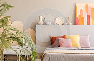 Colorful painting above bed with cushions in grey bedroom interior with palm. Real photo