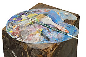 Colorful palette with brushes and painter`s knife on a rusty brown stand