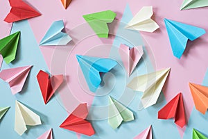 Colorful paper airplanes on pastel pink and blue colored background