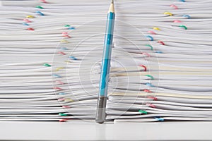 Colorful paper clip with pile of overload paperwork with pencil