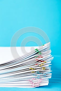 Colorful paper clip with pile of overload white paperwork on blue. Vertical foto