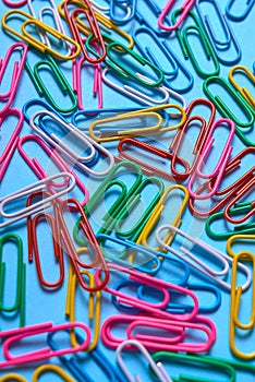 Colorful paper clips on blue pastel texture, copy space. Top view, flat lay. Back to school, business, education concept.