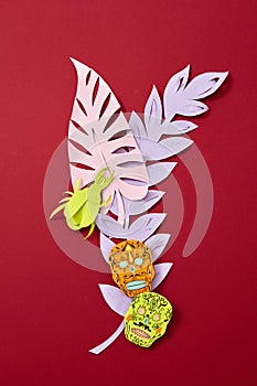 A colorful paper composition of various colored leaves and Calaveras attribute of the Mexican holiday of Calaca on a red photo