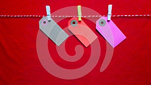 Colorful paper notes and clothespins on a red background. Empty color cardboard price tags, sale tag, gift tag, address label,