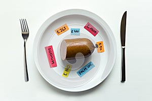 Colorful paper notes naming food additives and sausage on plate with fork and knife, food additive and unhealthy food concept