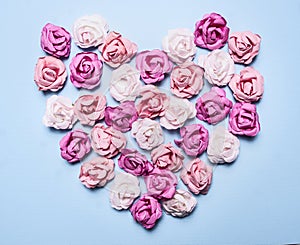 Colorful paper roses laid out in a heart shape on a blue background decorations Valentine's Day top view close up