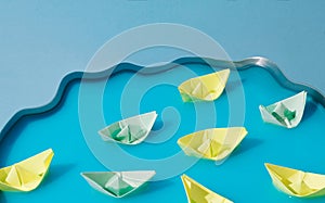 Colorful paper ships in blue water. Conceptual setting. Pastel background