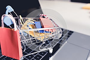 Colorful paper shopping bag in trolley on laptop. Customer can buy everything from office or home