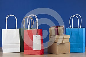 Colorful paper shopping bags on the floor against a blue paperwall background. Sale, consumerism, advertisement and retail concept