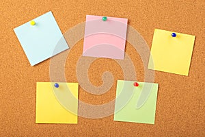 Colorful papers pined with tacks on brown cork board background photo