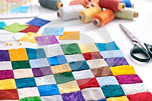 Colorful part of quilt sewn from square pieces, spools of thread, scissors, quilting and sewing accessories