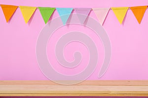 Colorful party flags hanging on pink background and wooden table