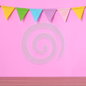 Colorful party flags hanging on pink background and wooden table