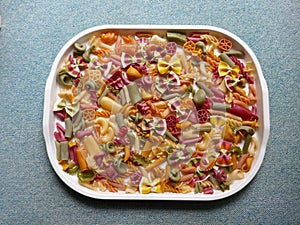 Colorful Pasta, Loop Noodles, Italian Pasta, Farfalle, Fusilli, Penne and others on a white tablet against a neutral background.
