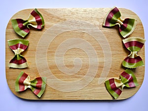 Colorful Pasta, Loop Noodles, Italian Pasta, Farfalle on a wooden board against a neutral background.