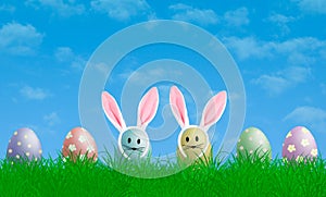 Colorful pastel easter eggs with bunny ears in grass with blue sky background, copy space