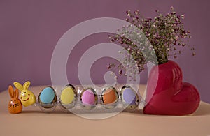 Colorful pastel Easter quail eggs in a row, two souvenir bunnies, a heart-shaped vase with pink gypsophila