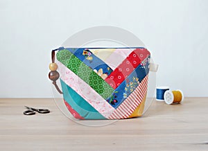 Colorful patchwork notions bag, retro scissors and thread spools on wooden desk