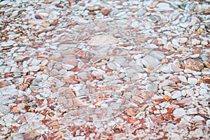 Colorful pebbles on the beach under the water. The wavy surface of the transparent sea water