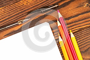 Colorful pencils, ballpoint pens, and white sheets of paper on a wooden table