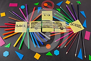 Colorful pencils in circles, titles Back to school and school bus drawn on the pieces of paper on the chalkboard