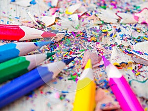 Colorful pencils with colorful pencil shavings on wooden background.