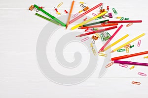 Colorful pencils and felt-tip pens, paper clips, stationery nails, smilie binders on white wooden background