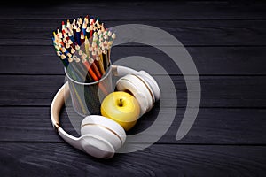 Colorful pencils and headphones on black wooden background. Workplace