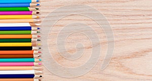 Colorful pencils lined up on oak wooden desktop