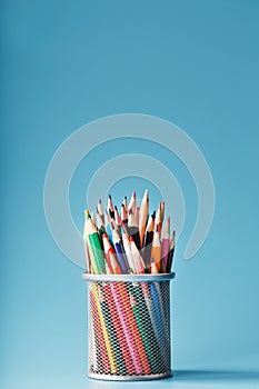 Colorful pencils in a metal jar on a blue background