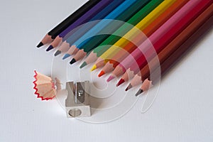 Colorful pencils with pencil sharpener on a sheet of white paperboard