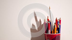 Colorful pencils in red glass on a white background with stark shadows