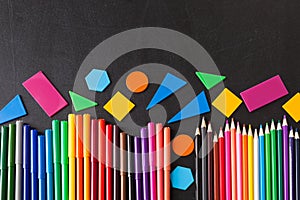 Colorful pencils in row and geometric figures on the black school chalkboard