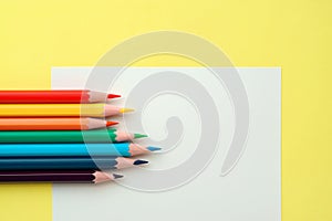 Colorful pencils on white paper on yellow background