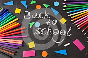 Colorful pens, pencils, title Back to school written by chalk and geometric figures on the chalkboard
