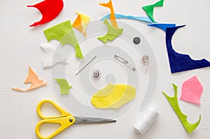 Colorful pieces of felt, scissors, needle, threads and pins on white wooden table. Table of seamstress. Craft concept. Colorful fl