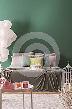 Colorful pillows and birthday cake with candles on king size bed in lovely bedroom, copy space on the empty wall