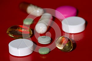 Colorful pills and capsules on a red surface .