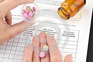 Colorful pills in hand and brown vial with medical questionnaire form on background