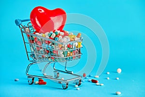 Colorful pills with red heart in shopping cart on blue background. concept: trade in medicines, pharmacies