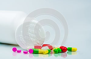 Colorful pills on white background and plastic bottle with blank label and copy space. Childproof packaging. Child resistant pill