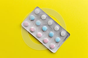 Colorful pills of white, blue and pink color in blister on yellow plain background.
