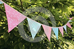 Colorful pink and blue triangular bunting flags hanging among trees. Summer garden party. Outdoor birthday or wedding