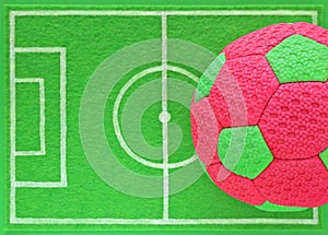 Colorful pink and green kids soccer ball on mini football field made of green felt, top view.